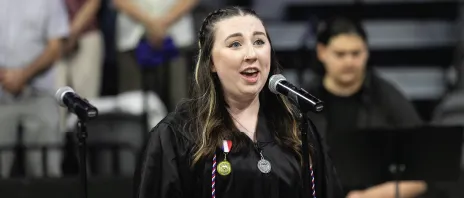 Student in graduation gown singing at commencement event.